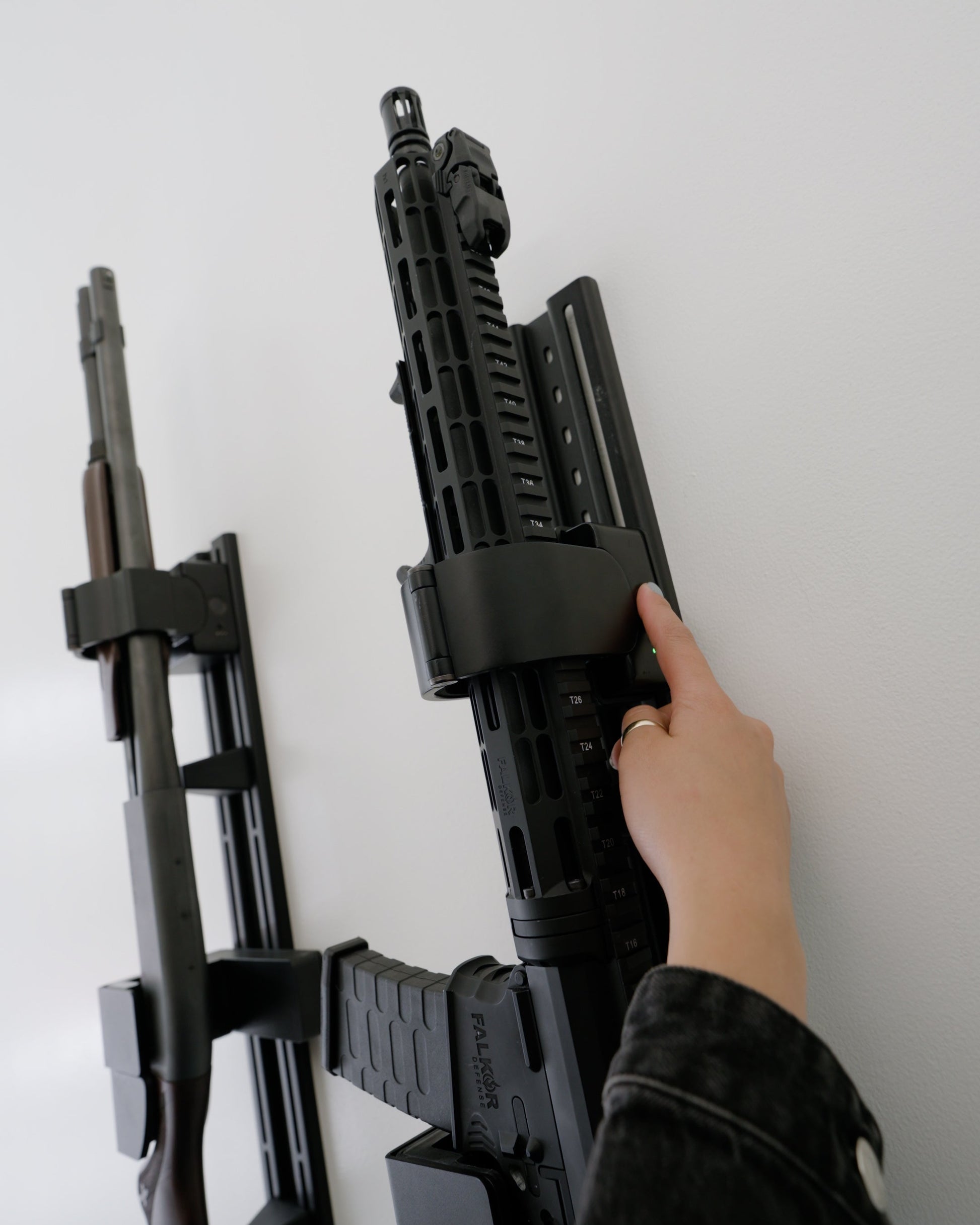 Person adjusting a mounted rifle against a white wall