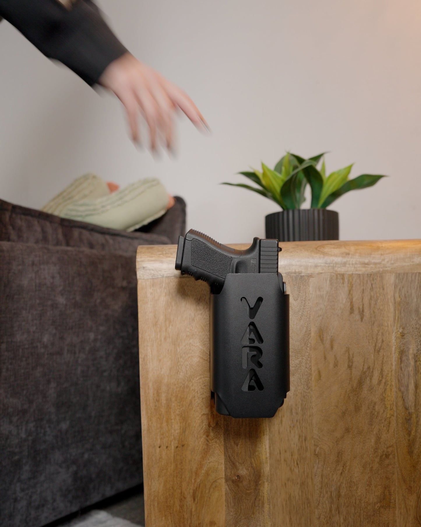 Reach Tactical handgun safe mounted on a nightstand beside a couch, holding a pistol with weapon-mounted light
