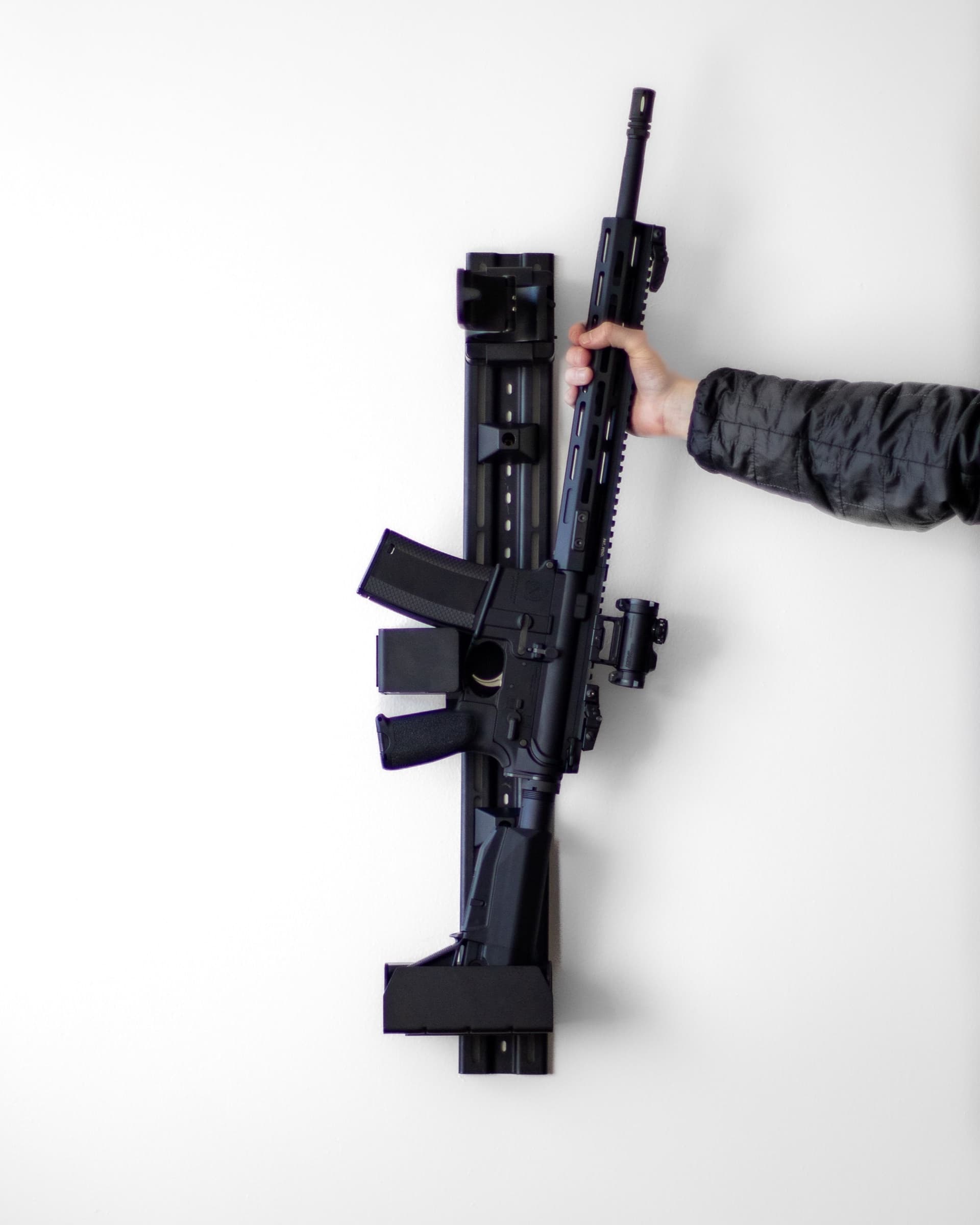 An AR-style rifle locked in a RACT safe on a white wall, a hand on the grip