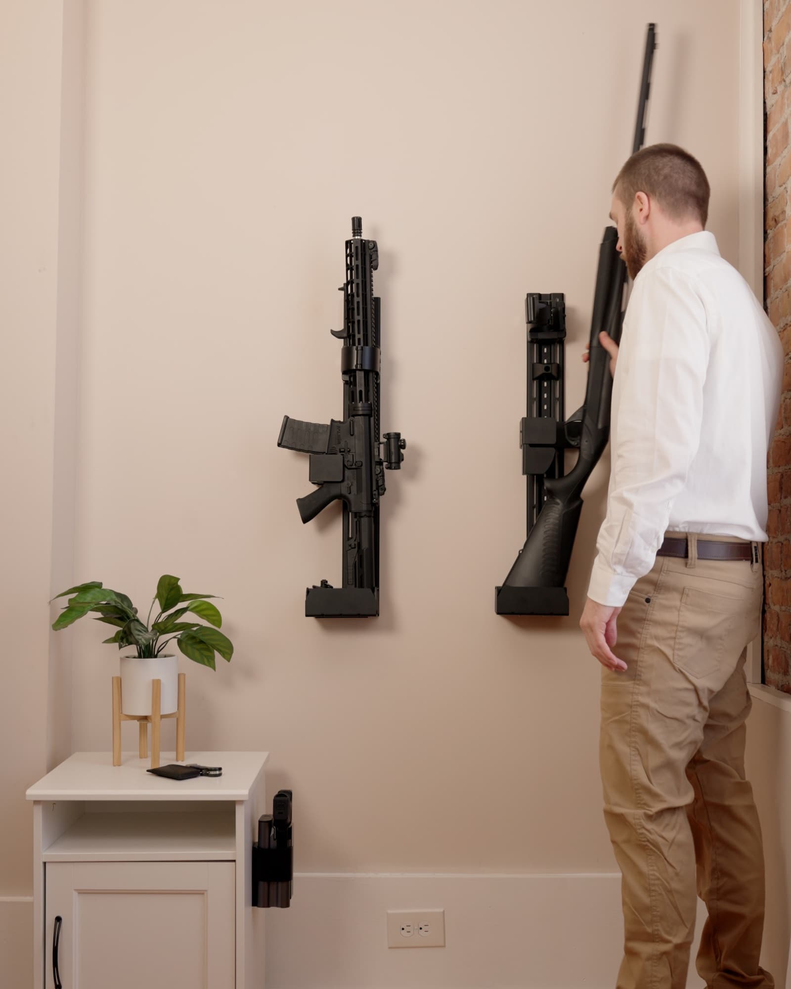 Two RACT safes on a wall holding an AR and a shotgun, a Reach safe on the side of the nightstand, and a man lifting the shotgun away