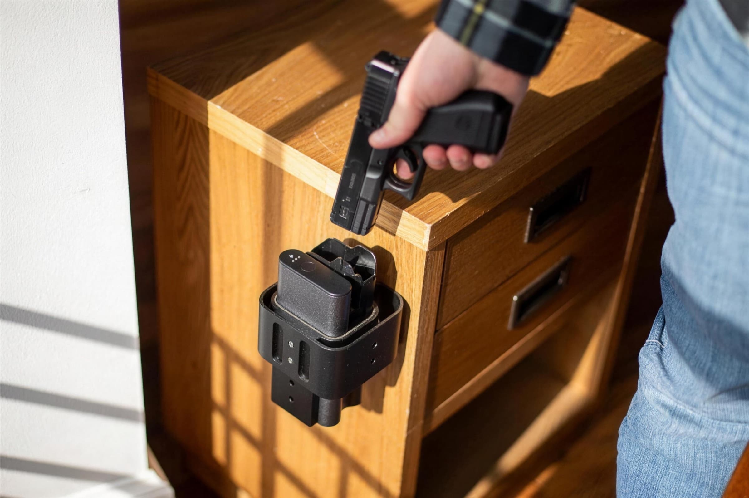A hand drawing a pistol from a Reach 2S mounted on the side of a wooden nightstand