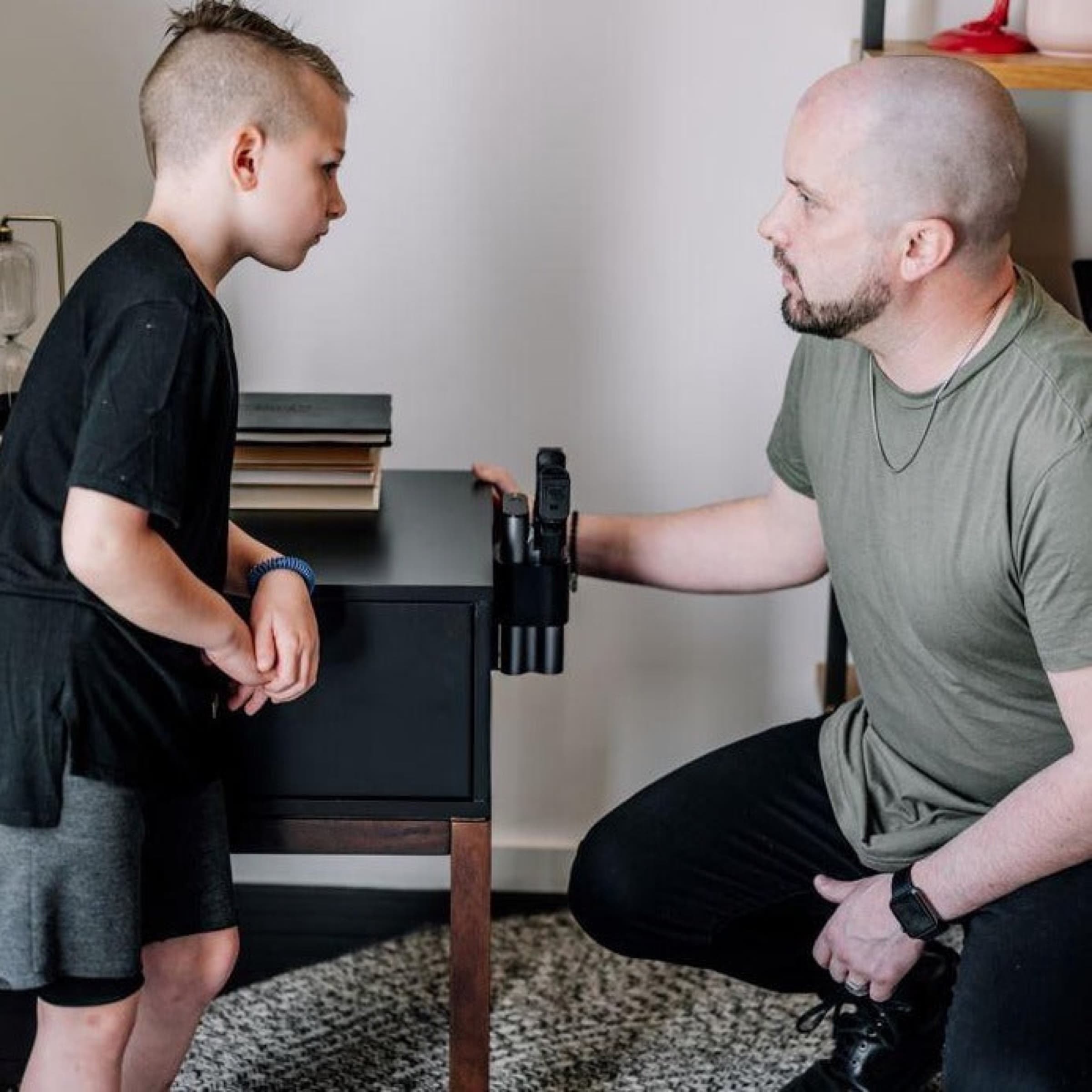 A father kneeling to talk with his son beside a nightstand with a Reach safe mounted on it