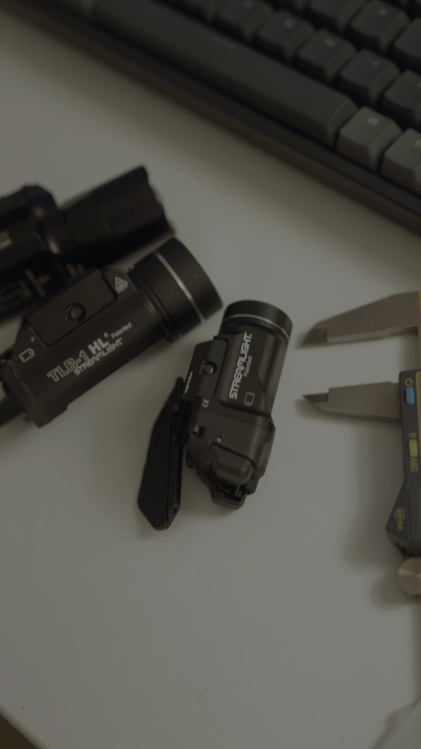 A pistol with a weapon-mounted light lying beside a second light and a knife on a desk