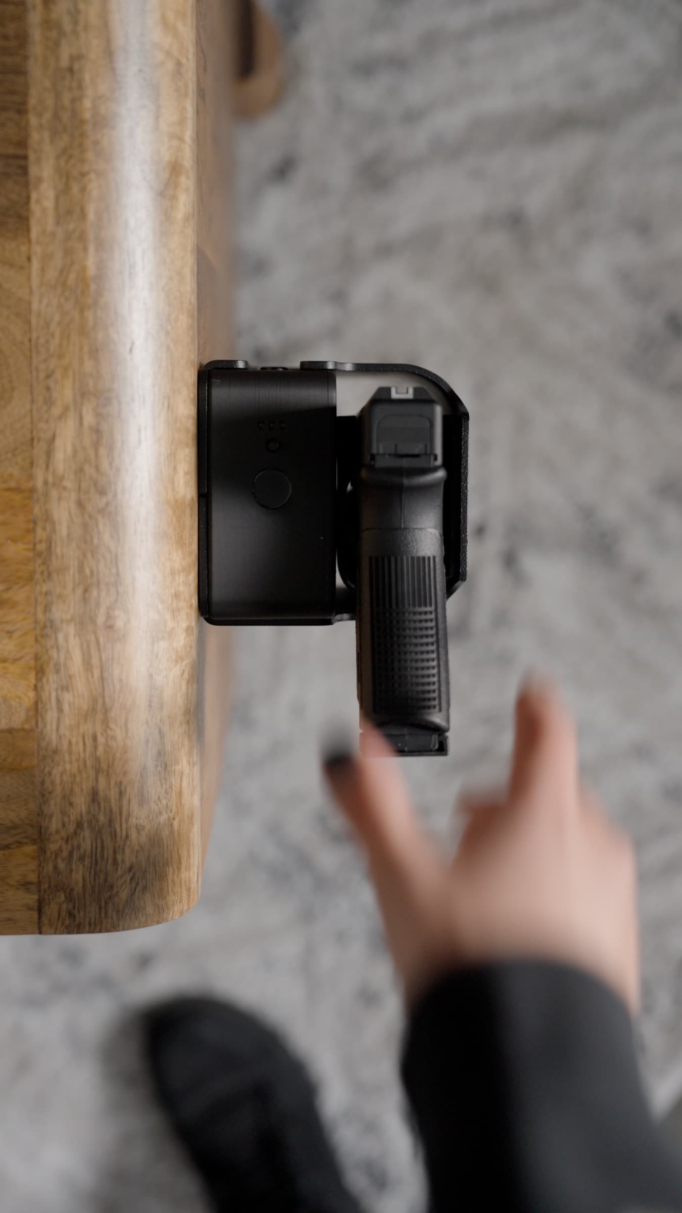 Seen from above, a hand reaching toward a pistol held in Reach Tactical on the side of a nightstand
