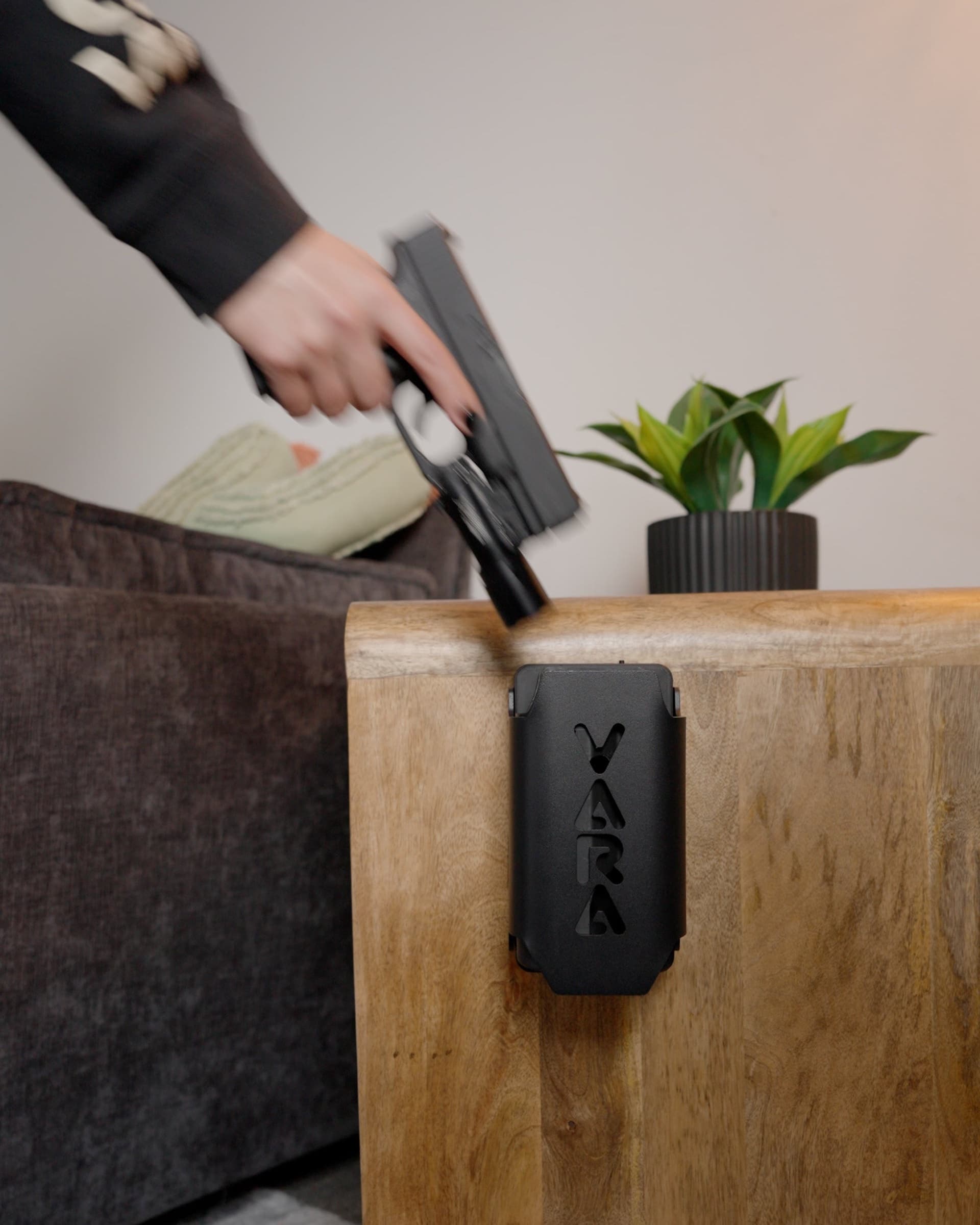A hand drawing a pistol up and out of a Reach safe mounted on a nightstand